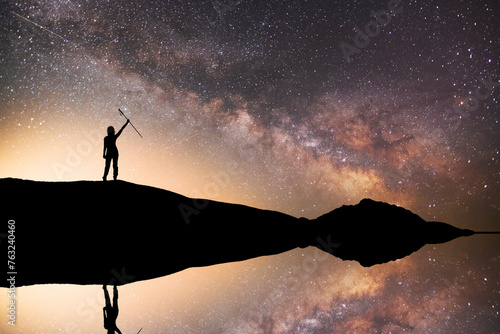 Silhouette of a hiker standing on the hill, on the milky way galaxy background.