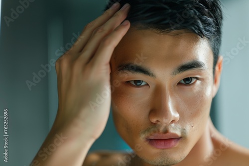 A close-up shot of a handsome Asian man admiring his smooth face in a handheld mirror, highlighting his perfect complexion. His gentle touch emphasizes his skin's radiance.