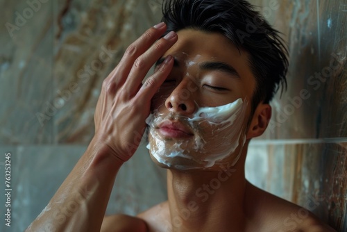 Detailed shot of a shirtless Asian man delicately patting a rejuvenating face mask onto his skin, promoting beauty and self-care.