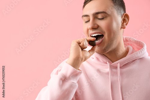 Young man eating heart-shaped chocolate candy on pink background, closeup © Pixel-Shot