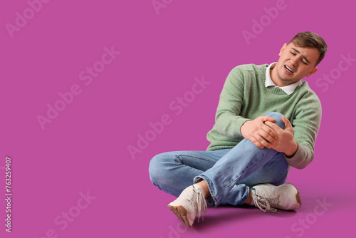 Tableau sur toile Young man suffering from knee pain on purple background