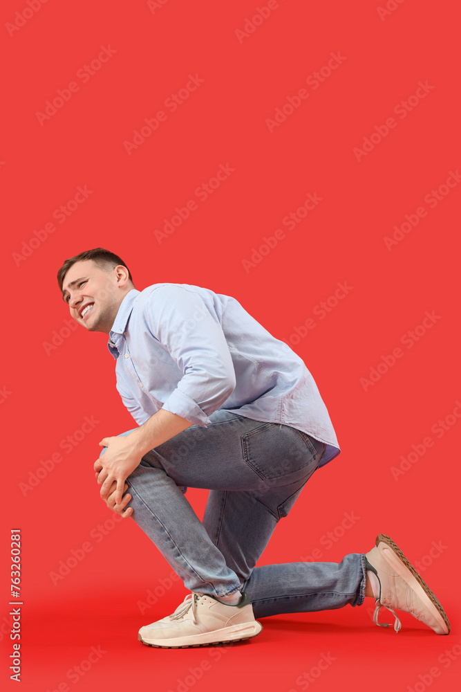 Young man suffering from knee pain on red background Young man suffering from knee pain on red background
