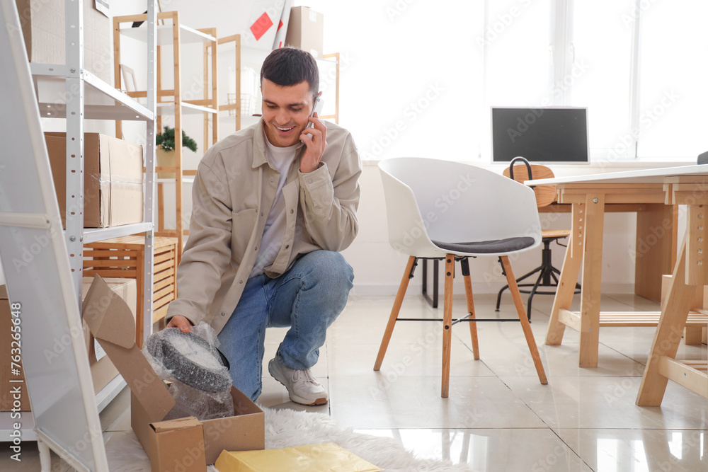 Male online store seller with wall clock talking by mobile phone in warehouse Male online store seller with wall clock talking by mobile phone in warehouse