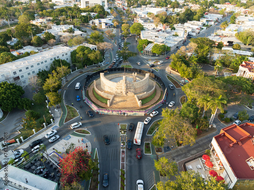 Aerial view of Paseo de Montejo, Monumento a la Bandera roundabout with traffic, trees, and shadows in evening, Merida, Yucatan, Mexico.