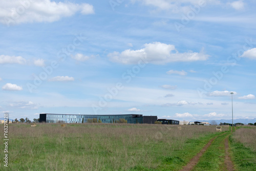 Obraz na płótnie Horizontal landscape - under the blue sky on the horizon the mirrored long modern building, seen across a field with green grass w salonie