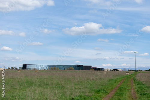 Obraz na płótnie Horizontal landscape - under the blue sky on the horizon the mirrored long modern building, seen across a field with green grass w salonie