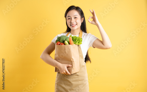 Portrait of an Asian girl holding a bag of fruits and vegetables on a yellow background