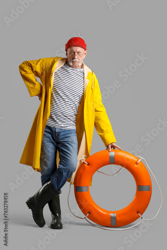 Mature sailor with ring buoy on grey background