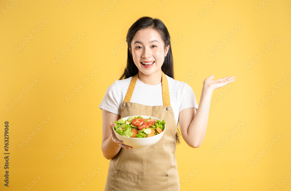 Portrait of Asian female housewife holding a bowl of salad and posing against a yellow background Portrait of Asian female housewife holding a bowl of salad and posing against a yellow background
