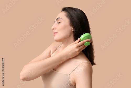 Beautiful young woman using hair scalp massager on brown background photo