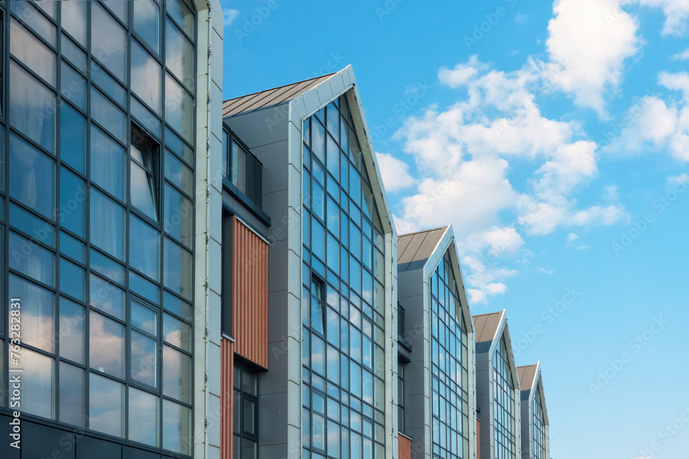 Fragment of the facade of a modern building. The glass windows reflect the blue sky with clouds. Background. Form. Fragment of the facade of a modern building. The glass windows reflect the blue sky with clouds. Background. Form.