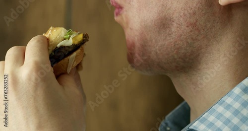 Close-up mouth of a hungry man with braces on his teeth greedily bites his hamburger, eats hamburger in a restaurant, enjoying a delicious juicy burger, an adult guy appetizingly bites a hamburger. 4k photo