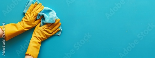 Hands with Yellow Cleaning Gloves and Blue Cloth on Blue Background