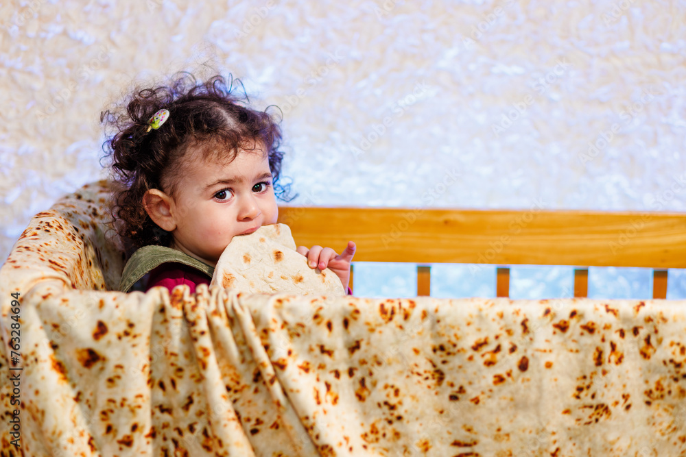 Cute curly hair girl eating Armenian bread lavash in her crib