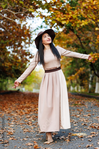 Obraz na płótnie Cute young woman with wide-brimmed hat and fashionable attire standing on pathway surrounded by fall trees w salonie