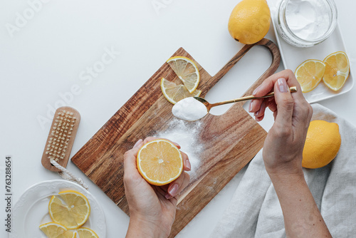 wooden cutting board with soda and lemons on a white background. a woman's hand with a lemon and a golden spoon with soda cleans it. rectangular plate with a can of soda and lemons