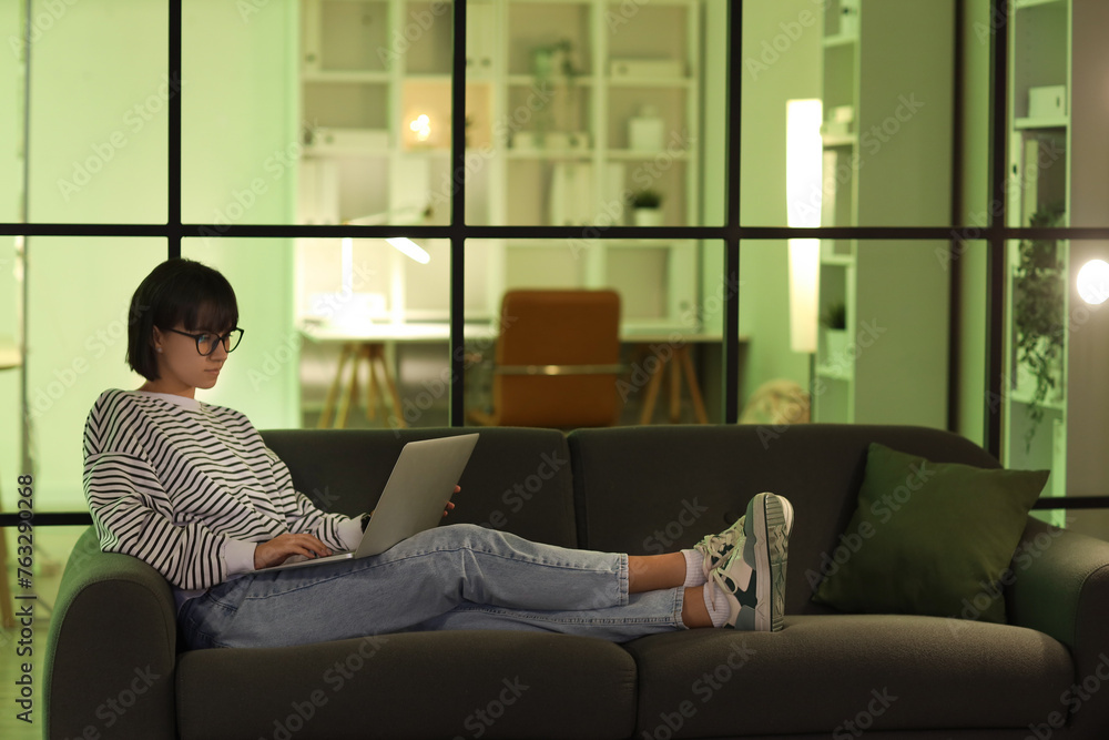 Female programmer working with laptop on couch in office at night Female programmer working with laptop on couch in office at night