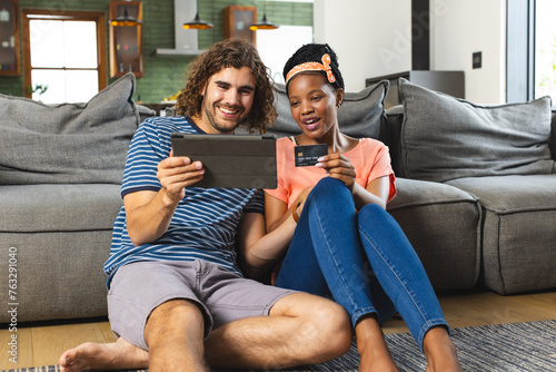A diverse couple is shopping online with a tablet at home