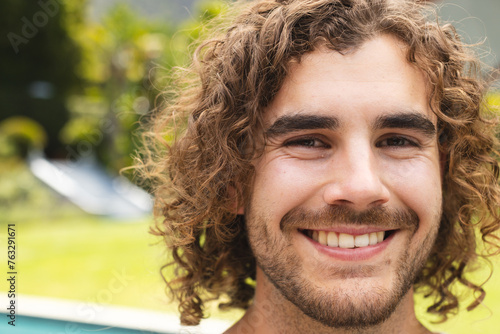 A young Caucasian man smiles broadly outdoors, showcasing curly brown hair at home