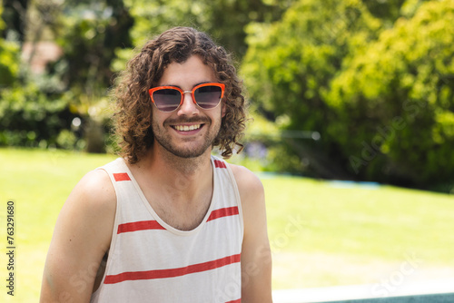 A young Caucasian man with curly hair smiles outdoors with copy space at home