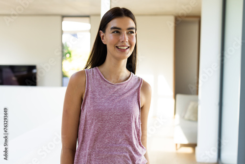 A young Caucasian brunette woman stands smiling in a bright room at home