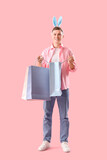 Young man in bunny ears with shopping bags on pink background. Easter Sale