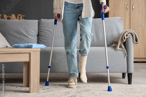 Obraz na płótnie Injured young woman with crutches after accident walking at home