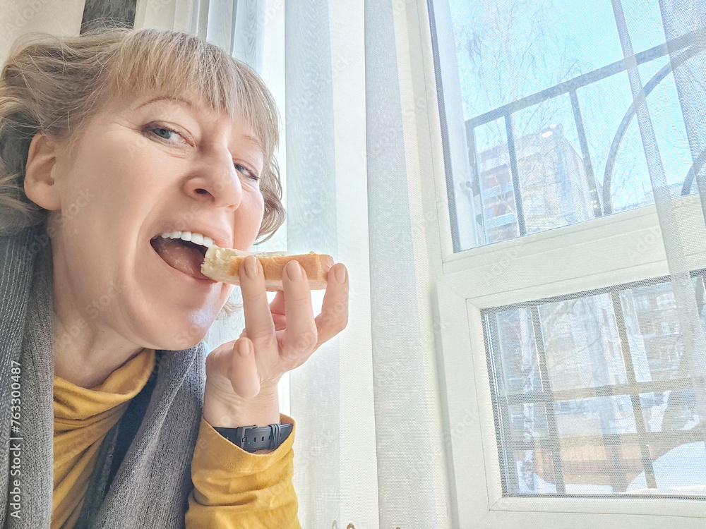 Mature Woman Enjoying Light Breakfast With Coffee by the Window. Woman in with morning coffee and bread. A blogger takes a selfie while eating Mature Woman Enjoying Light Breakfast With Coffee by the Window. Woman in with morning coffee and bread. A blogger takes a selfie while eating