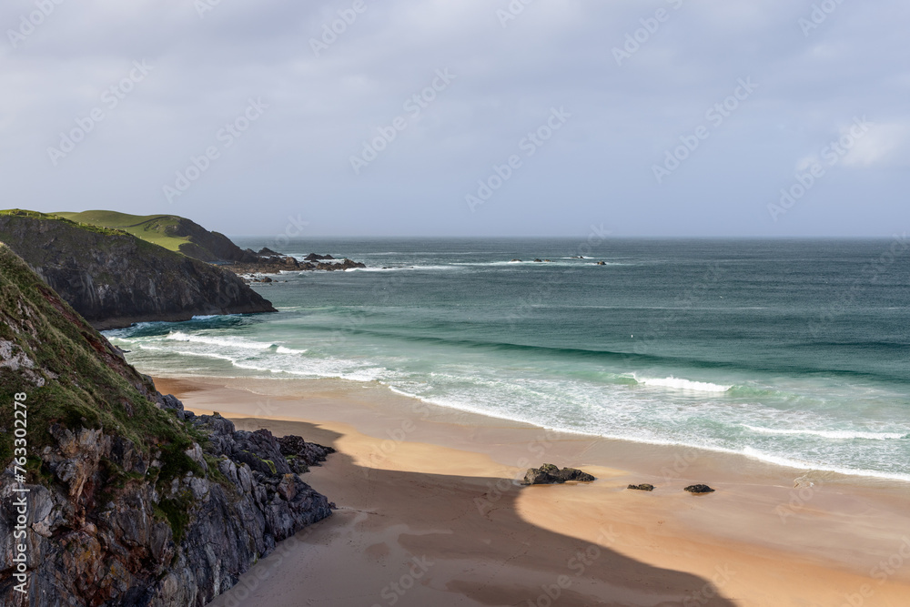 A dramatic view of Durness Beach in Scotland, where rugged cliffs meet the pristine sands and the emerald waves of the Atlantic