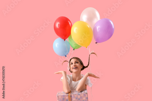 Young woman with balloons and gift box on pink background