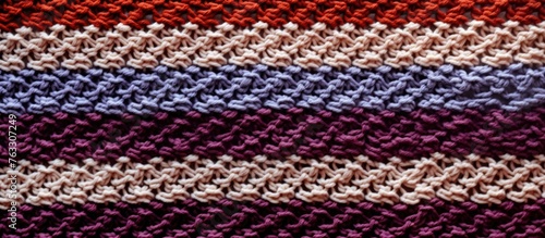 A close up of a purple knitted textile rectangle blanket with a creative arts striped pattern in violet, magenta, and electric blue colors. Made of woolen material with symmetrical design