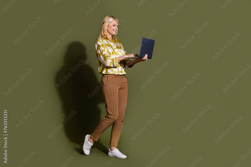 Full length photo of businesswoman in stylish yellow shirt using netbook information tech make sales isolated on khaki color background Full length photo of businesswoman in stylish yellow shirt using netbook information tech make sales isolated on khaki color background