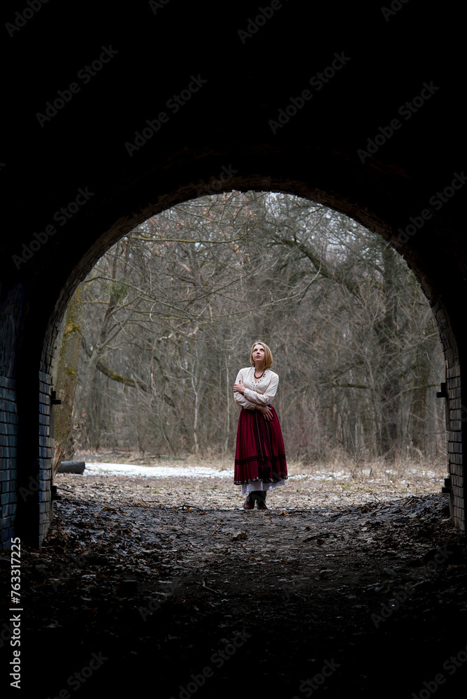 dark silhouette of dramatic lonely single woman in stone arch in winter forest