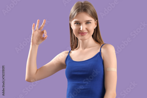 Pretty young woman with applied medical patch showing OK gesture on lilac background