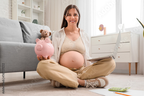 Young pregnant woman with piggy bank and laptop at home. Maternal Benefit con...