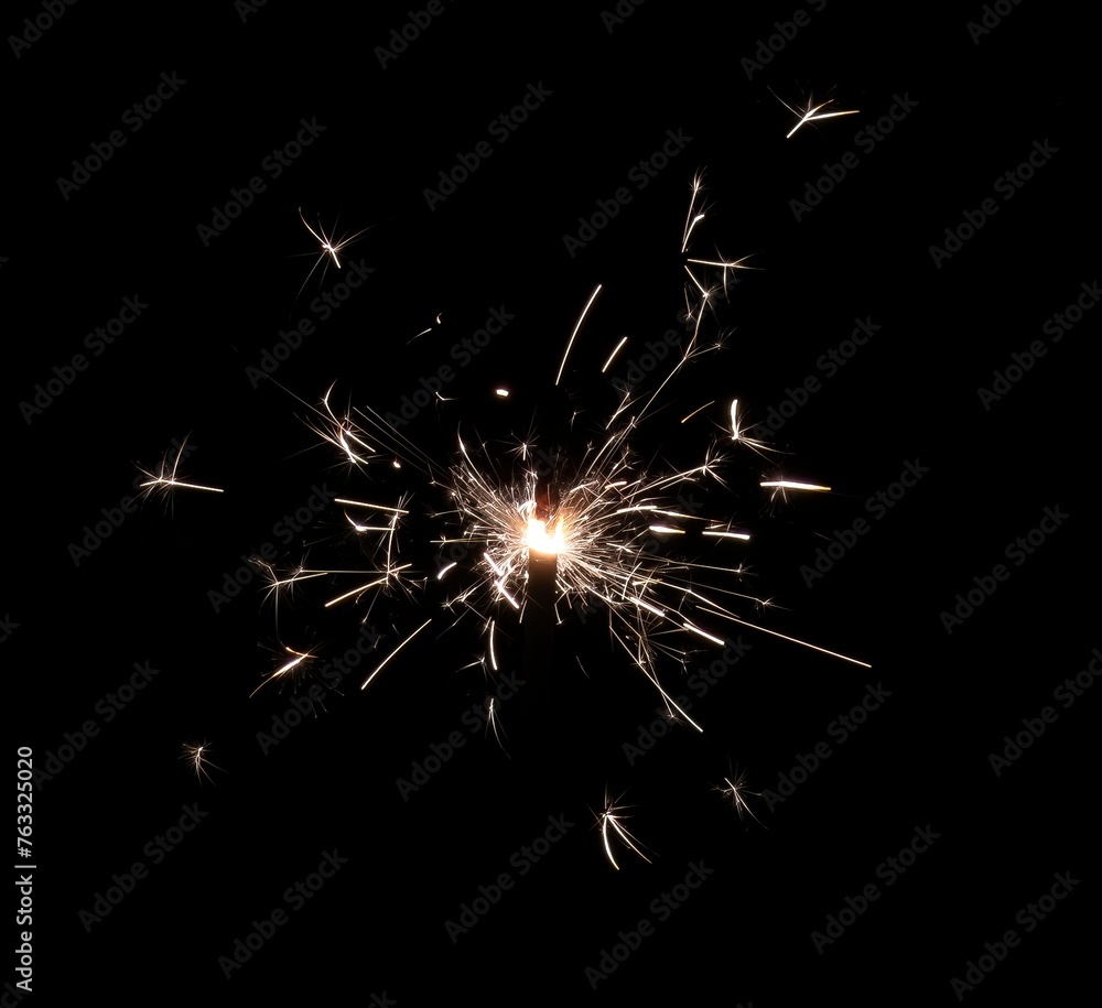A burning sparkler that shoots hot and bright sparks on a black background