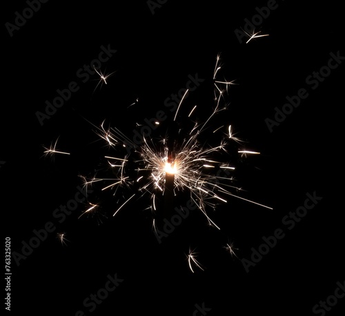 A burning sparkler that shoots hot and bright sparks on a black background