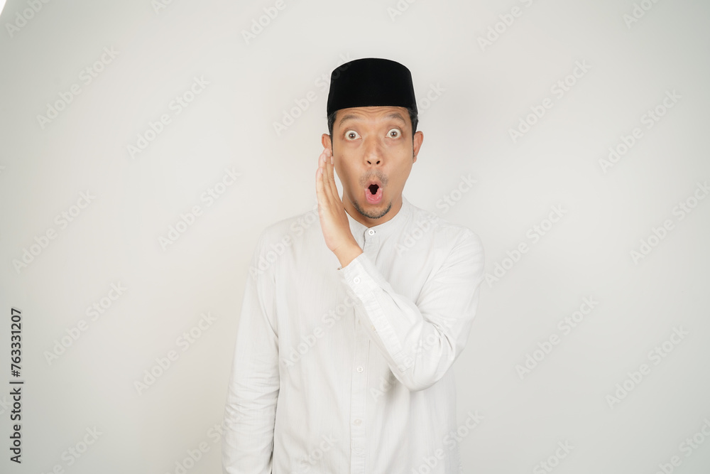 Asian Muslim man telling secrets in mouth, whispering gossip, wearing Arab costume at copy space on isolated background Asian Muslim man telling secrets in mouth, whispering gossip, wearing Arab costume at copy space on isolated background