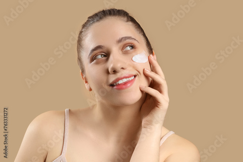Young woman with facial cream on beige background, closeup