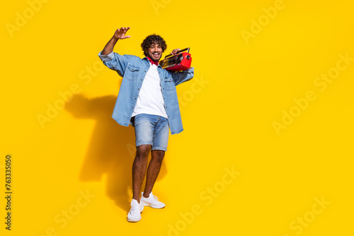 Full body photo of attractive young man boombox music cheerful wear trendy denim clothes red scarf isolated on yellow color background
