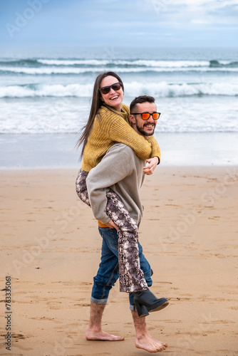 A young couple looking at camera while laughing and playing in the beach in winter. photo