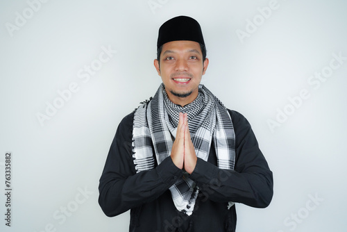 Happy smiling Asian Muslim man in Arabic turban sorban standing with Eid greeting gesture and welcoming Ramadan isolated background photo