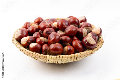 A straw basket of freshly picked up chestnuts to roast by a fire isolated on white