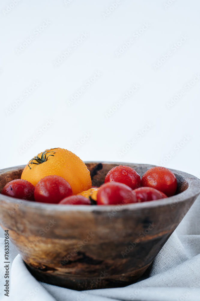 red and yellow tomatoes covered with water drops in a wooden bowl on a white background red and yellow tomatoes covered with water drops in a wooden bowl on a white background