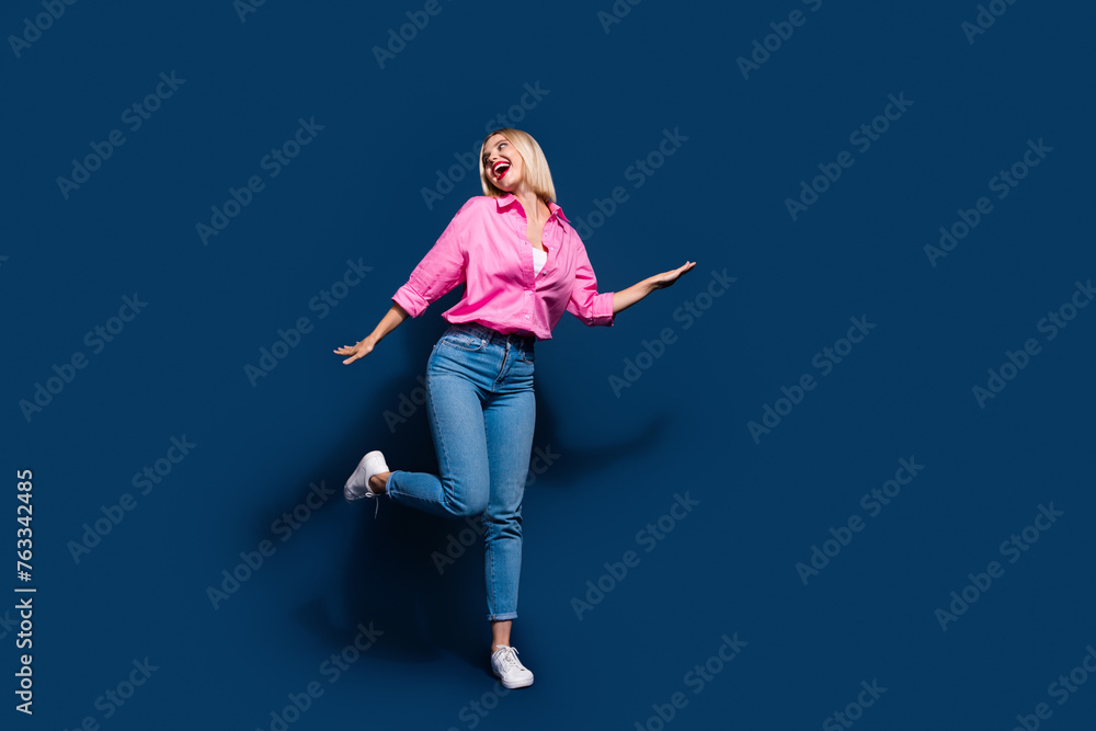 Full size photo of gorgeous girl dressed pink shirt jeans dancing look at event promo empty space isolated on dark blue color background