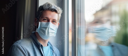 Man in mask looking out window, senior man smiling by window during quarantine photo
