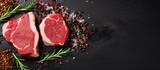 Two raw beef steaks with spices on black background