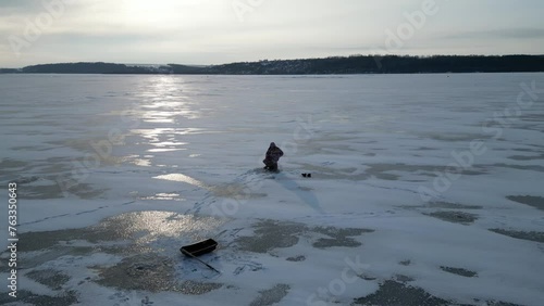 Bird's eye view of a lake that is covered with ice. A fisherman catches fish on the ice.