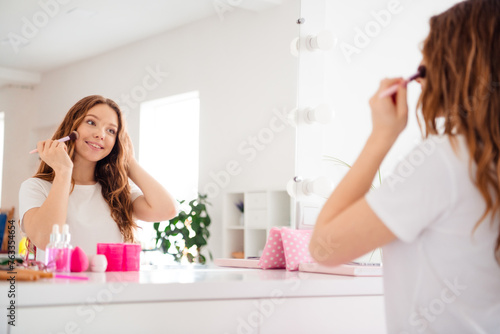 Portrait of cheerful gorgeous girl apply face highlighter powder look mirror reflection bright interior bedroom inside