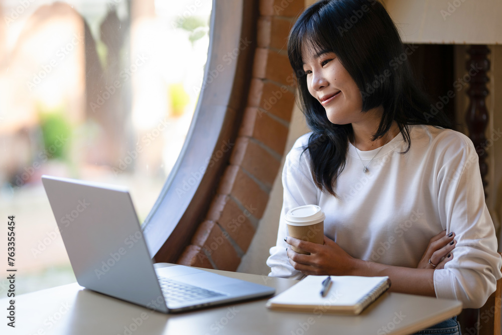 Young Asian woman taking a coffee break while working remotely in a coffee shop. Young Asian woman taking a coffee break while working remotely in a coffee shop.